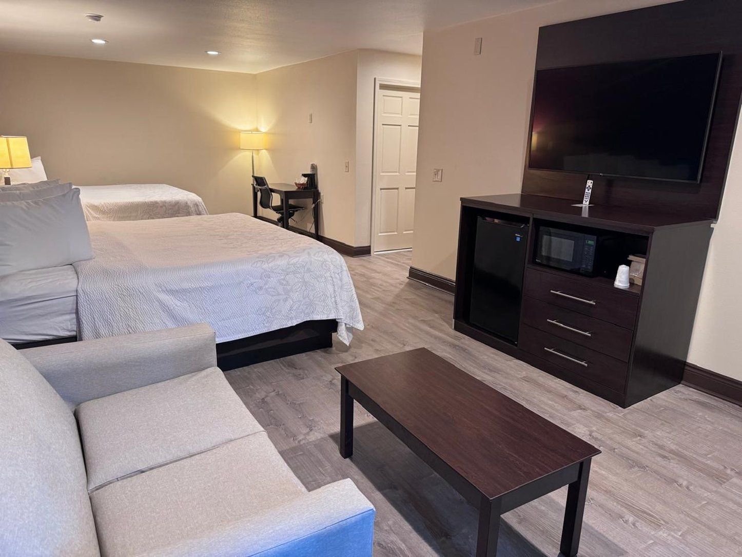 Quarto de hotel com cama, sofá, escrivaninha com televisão e micro-ondas.