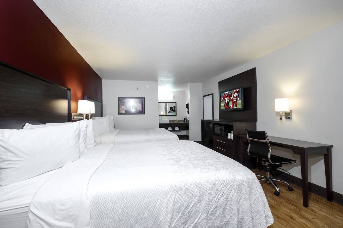 A hotel room with a large bed, a desk, a chair, a television, and a mirror.