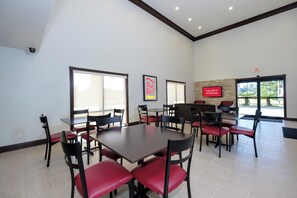 A hotel dining area with multiple tables and chairs, a mounted television, and an exit sign. - Red Roof Inn PLUS+ Hammond (Hammond)