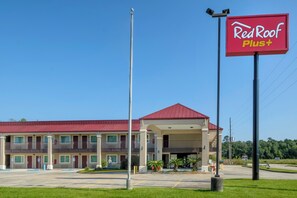 A Red Roof Plus hotel with a red roof, a covered parking area, and a clear blue sky. - Red Roof Inn PLUS+ Hammond (Hammond)