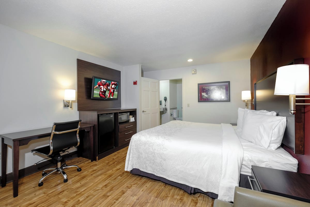 A hotel room with a bed, desk, chair, television, and artwork on the walls.
