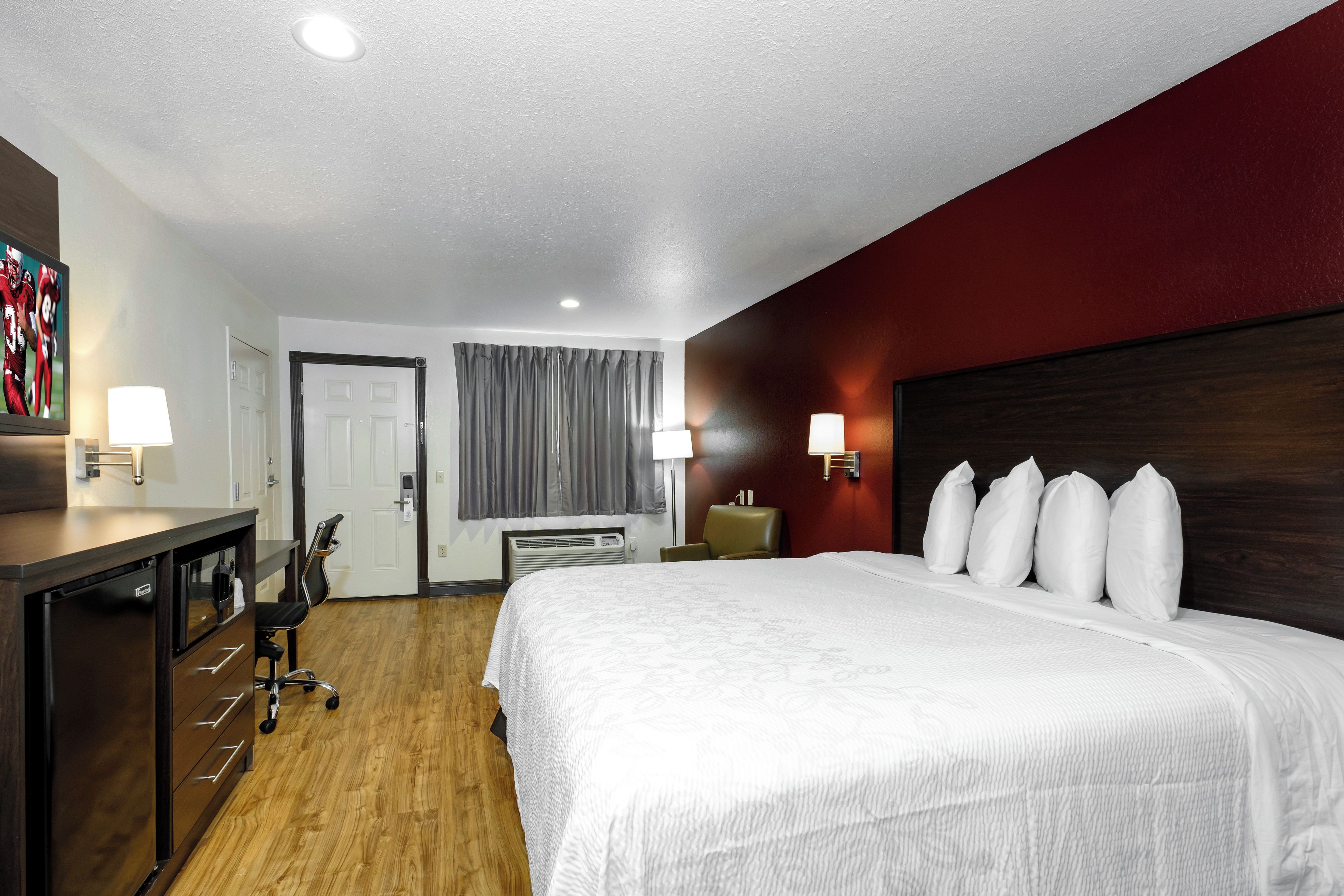 A hotel room with a bed, desk, chair, and two wall-mounted lamps.