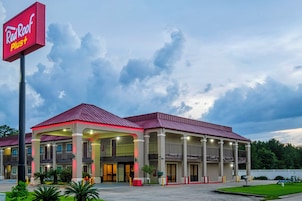Hotel Red Roof Plus com área de estacionamento coberta e um grande letreiro.