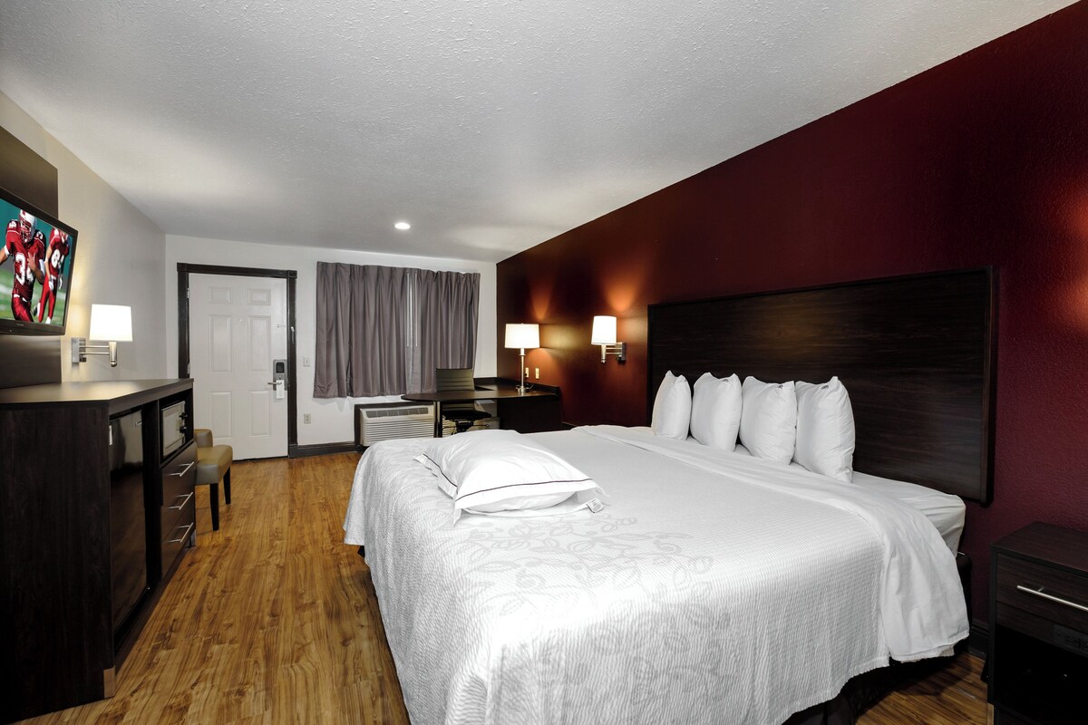 A hotel room with a bed, bedside tables, a desk, a chair, a television, and a window with curtains.