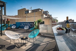 En tagterrasse med udendørs siddepladser, et barområde og udsigt til bygningen med teksten 'JAZZ BCN'.