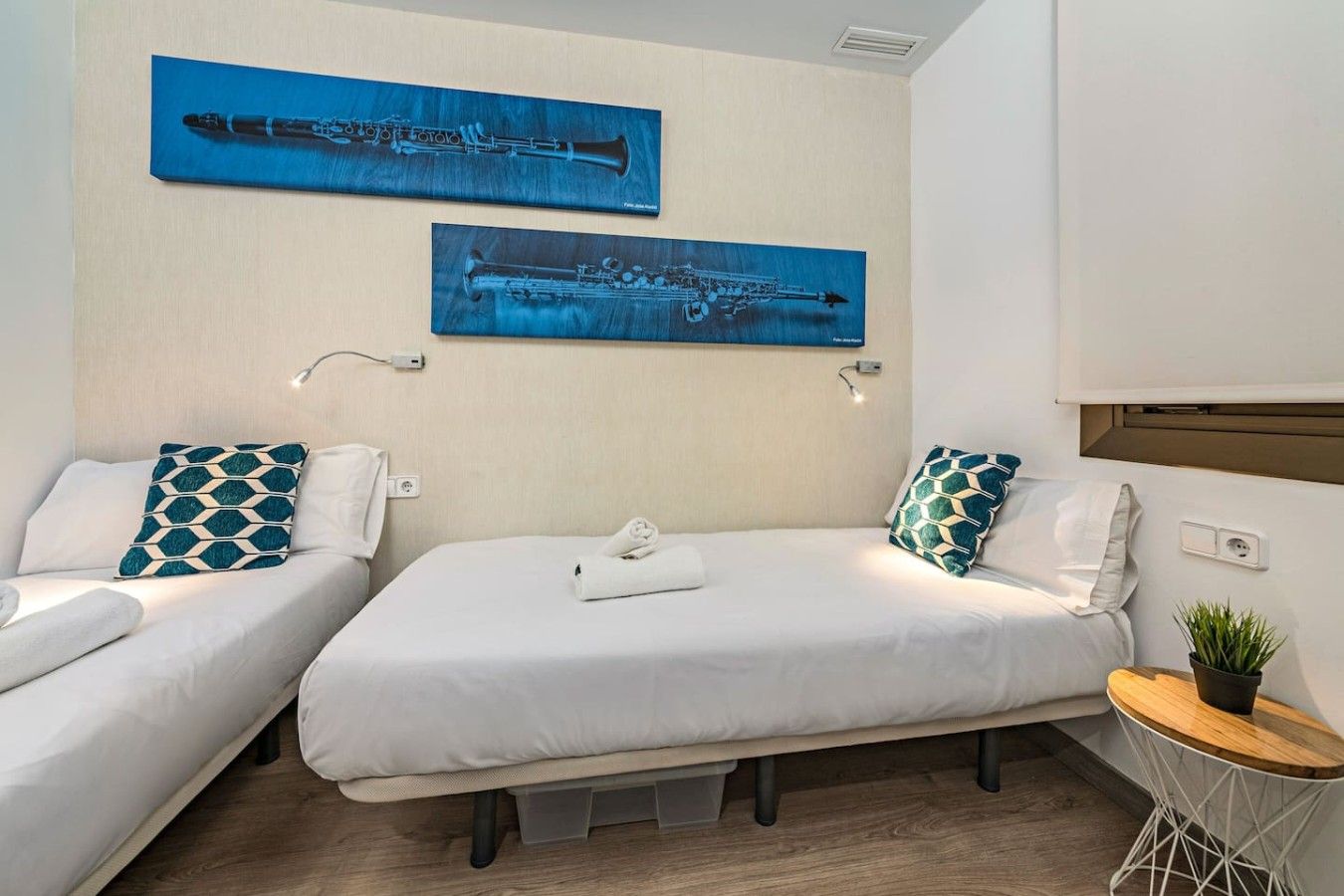 A hotel room with two beds, each with a pillow and a rolled towel. There are two wall-mounted paintings above the beds.