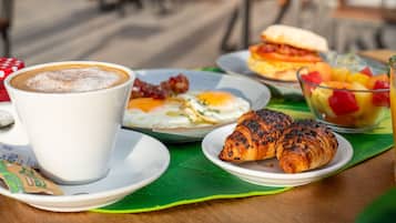 A breakfast setting with coffee, eggs, croissants, and fruit on a table.