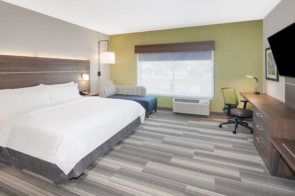 A hotel room with a large bed, a desk, a chair, and a window with a view of the street.