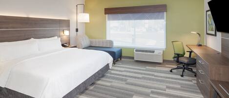 A hotel room with a large bed, a desk, a chair, and a window with a view of the street.