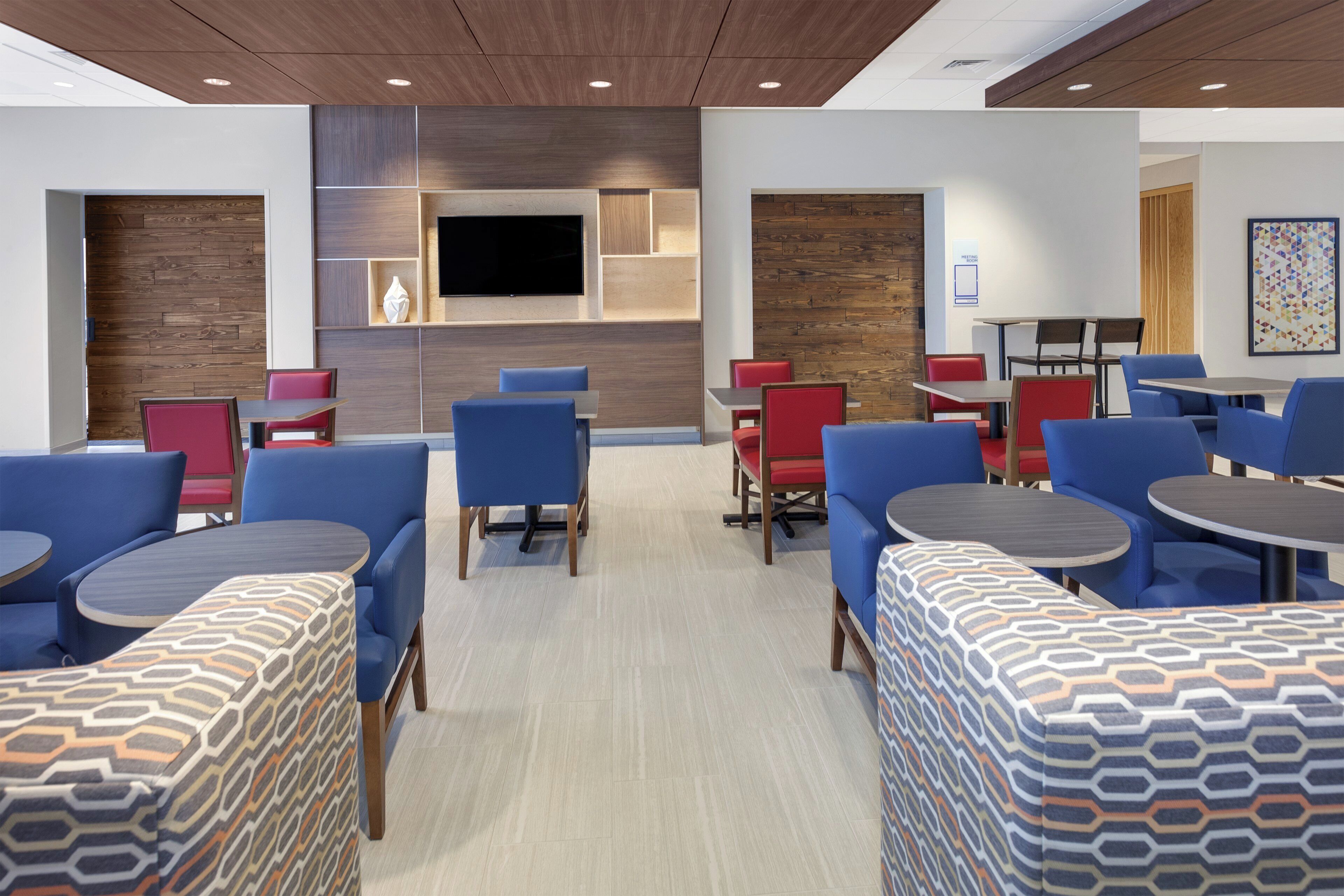 A modern hotel lobby with seating areas, a flat-screen TV, and a meeting room sign.