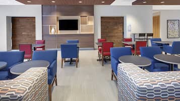 A modern hotel lobby with seating areas, a flat-screen TV, and a meeting room sign.