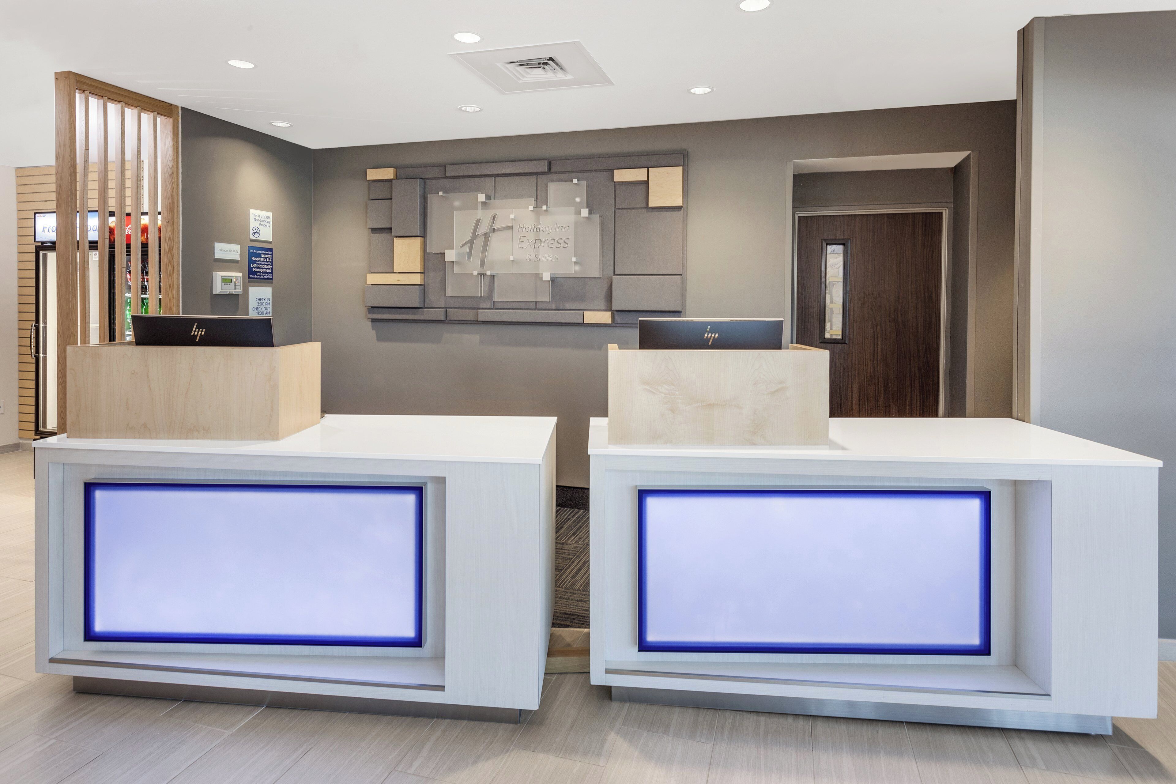 A hotel reception area with two reception desks, a digital display, and a wall-mounted sign.
