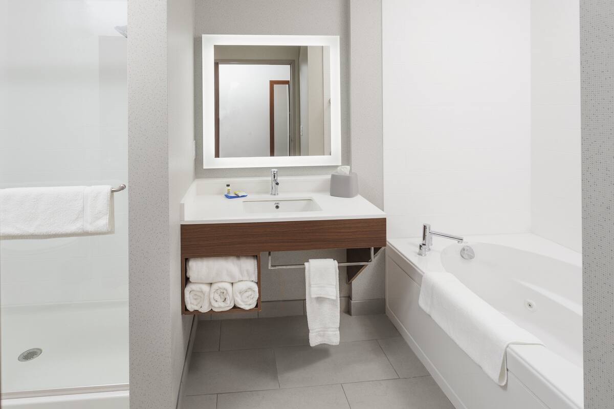 A modern bathroom with a white sink, mirror, and bathtub. There is a towel rack with folded towels and a shower area.