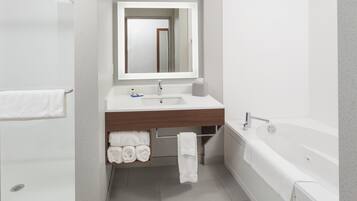 A modern bathroom with a white sink, mirror, and bathtub. There is a towel rack with folded towels and a shower area.