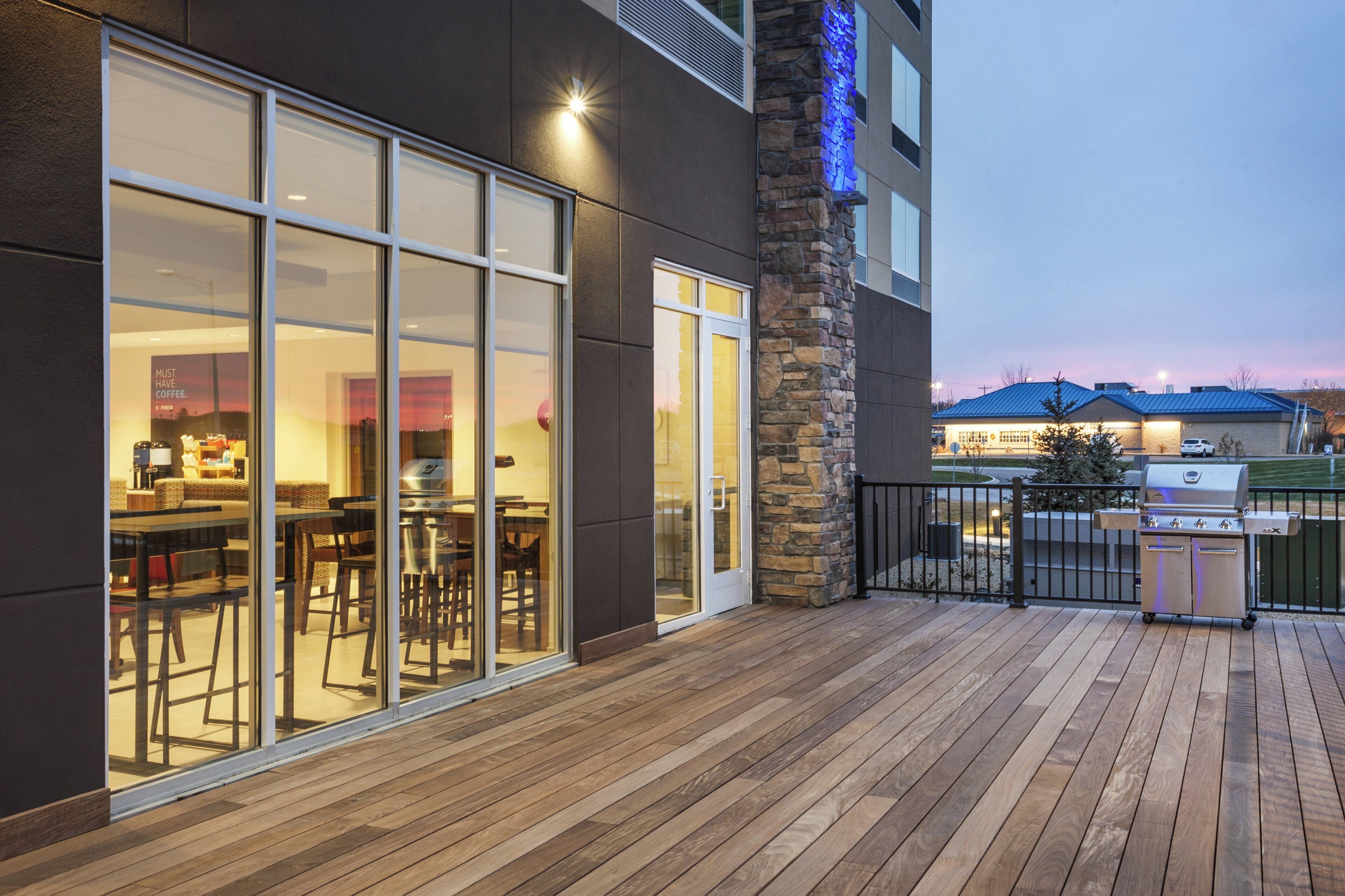 A wooden deck with a barbecue grill, a stone pillar, and a glass door leading to an indoor dining area.
