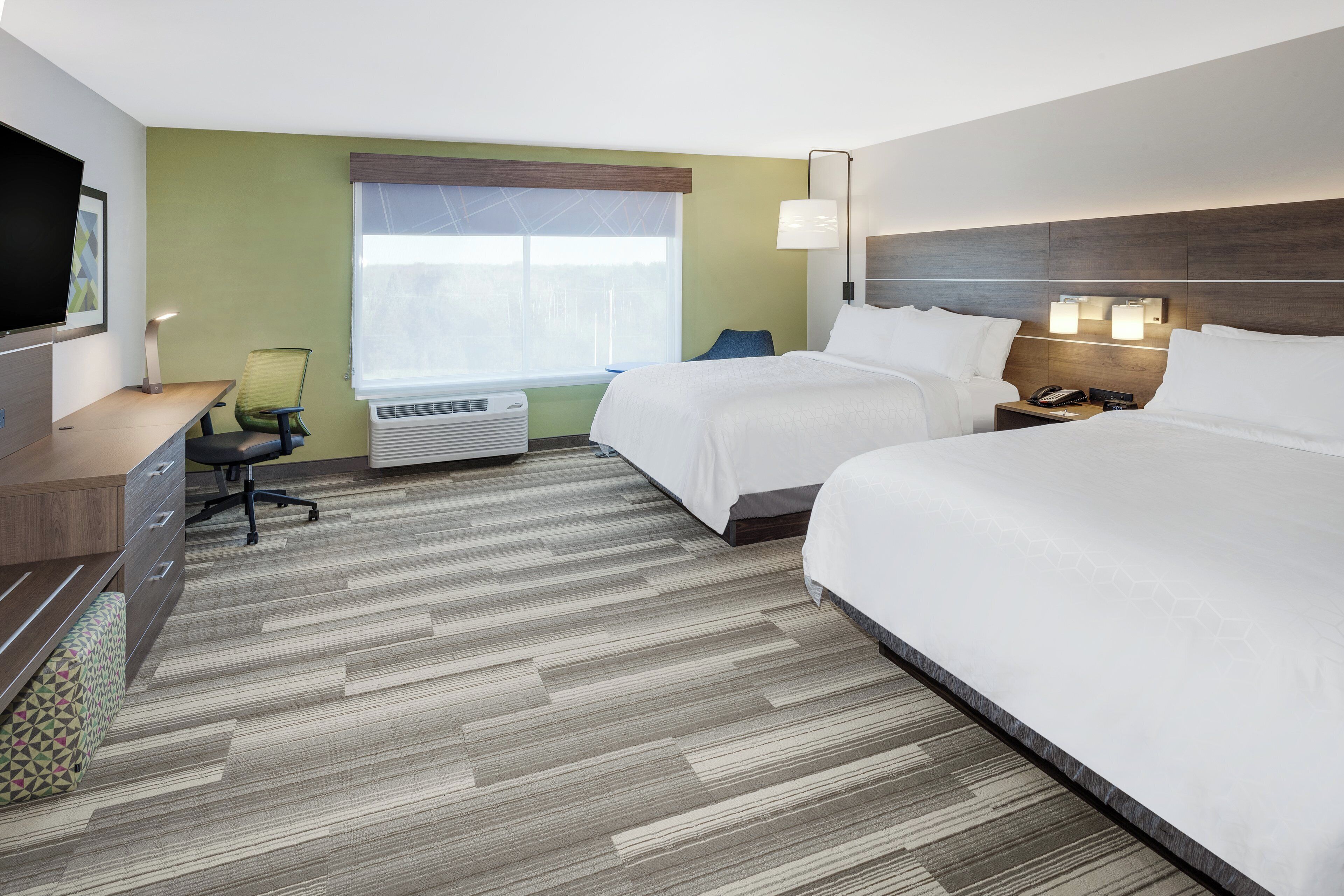 A hotel room with two beds, a desk, a chair, a TV, and a window with blinds.