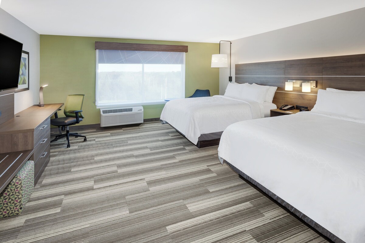 A hotel room with two beds, a desk, a chair, a TV, and a window with blinds.
