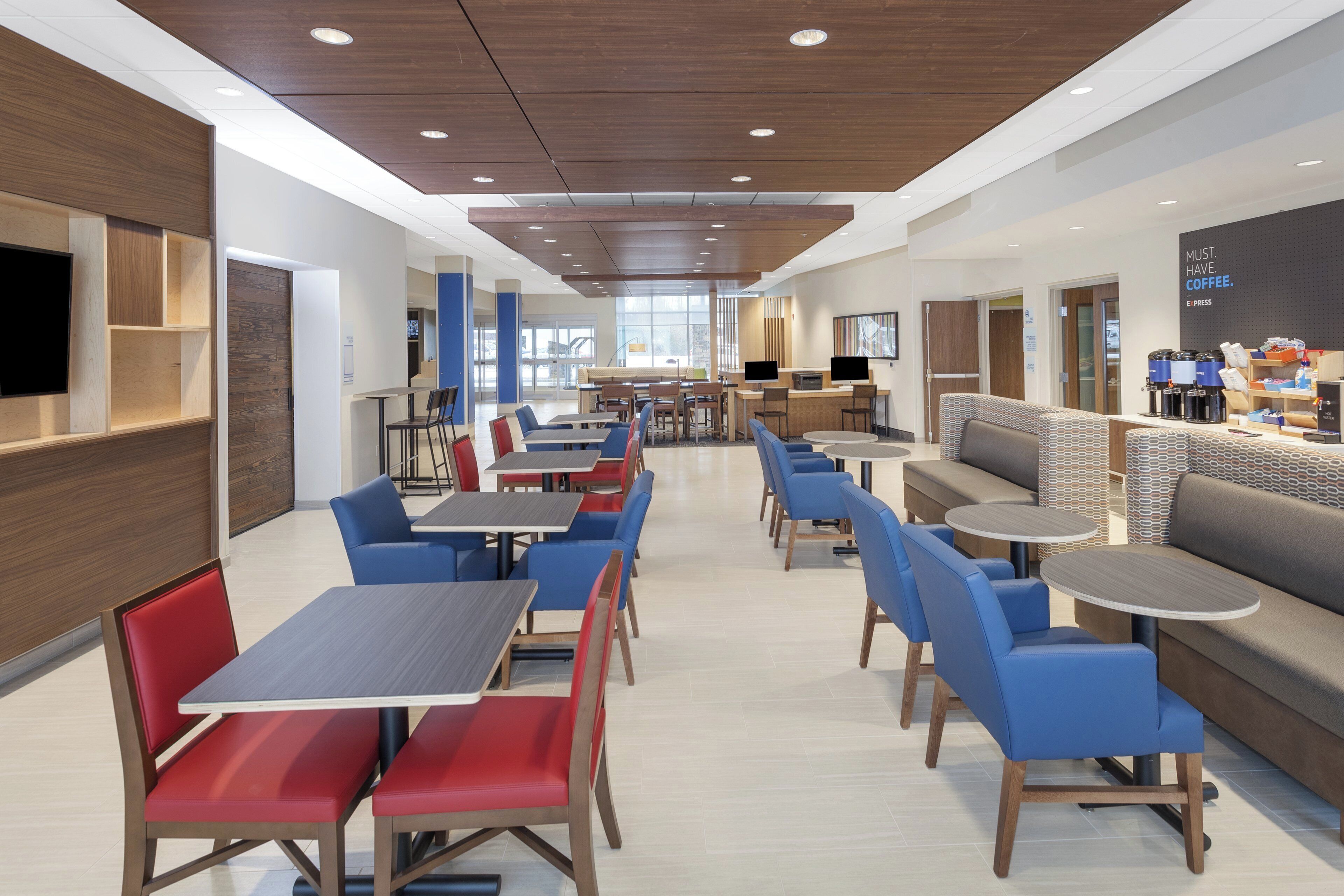 A modern hotel lobby with seating areas, a coffee station, and a large TV screen.