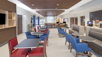 A modern hotel lobby with seating areas, a coffee station, and a large TV screen.