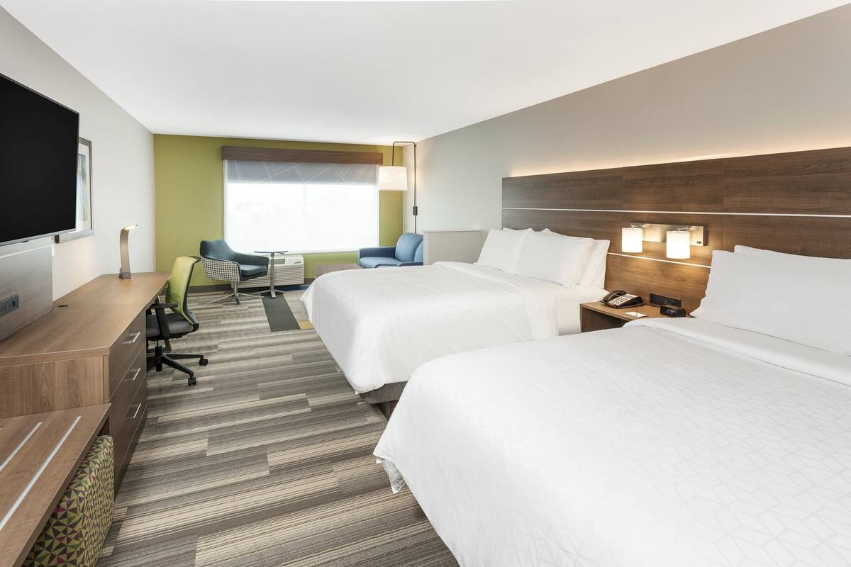 A hotel room with two beds, a desk with a chair, a TV, and a window with blinds.