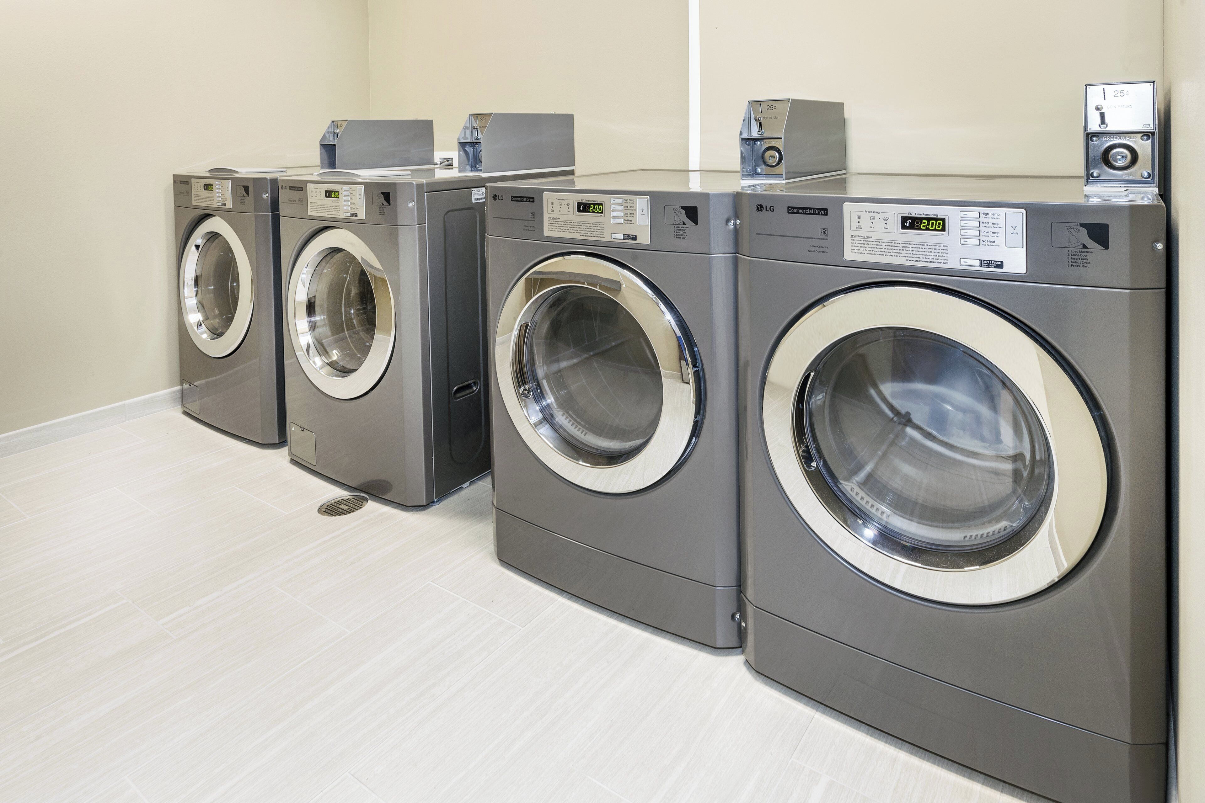 Une rangée de quatre sèche-linge commerciaux LG à chargement frontal dans une buanderie.