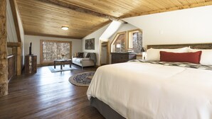 Quarto com cama grande, teto de madeira e vista para o exterior através de uma janela.
