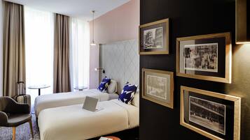 A hotel room with two beds, a desk, a chair, and a small table. There are framed pictures on the wall.