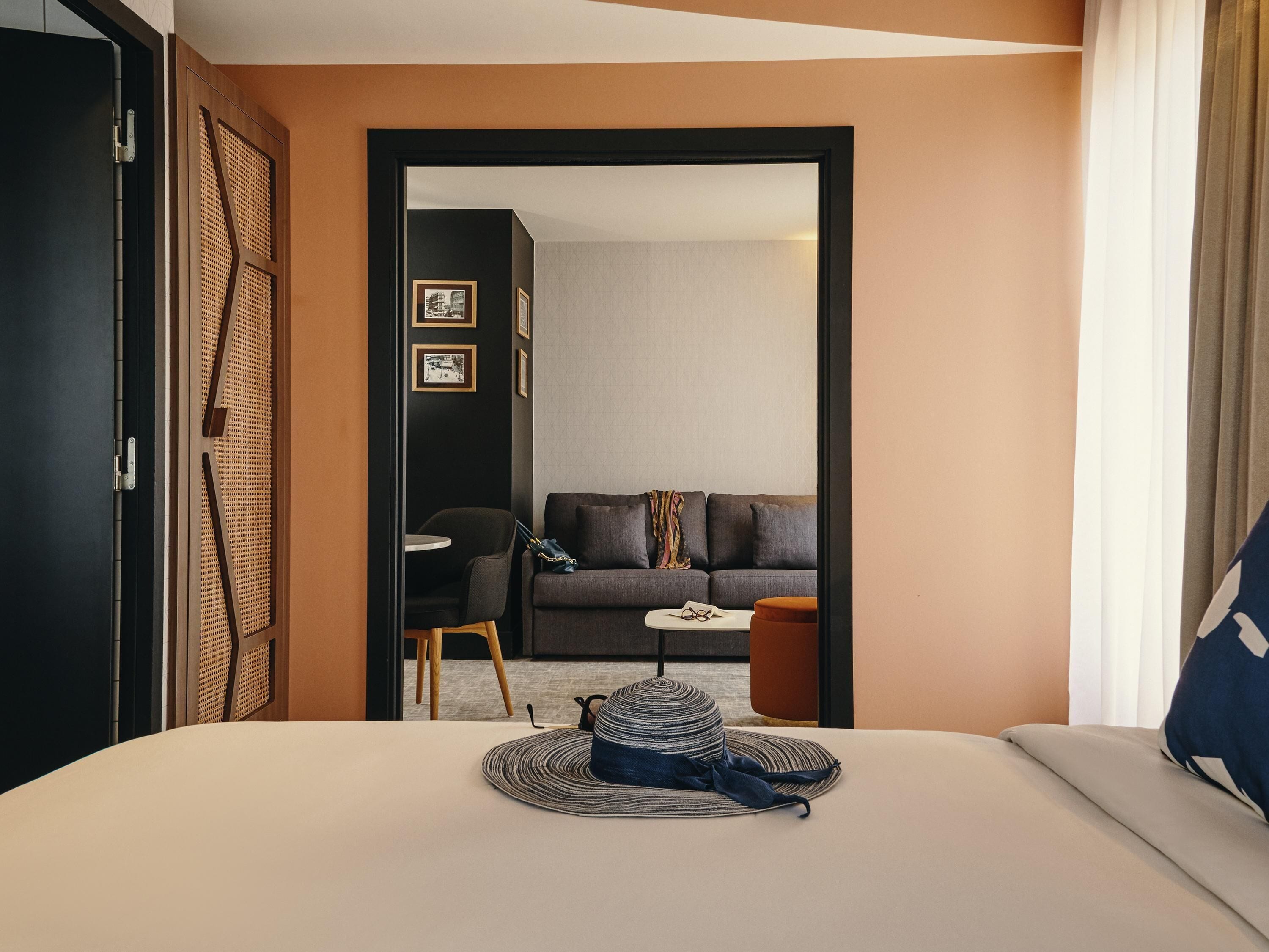 Une chambre d’hôtel comprenant un lit, une petite table, une chaise, un canapé et une porte donnant sur une autre pièce.