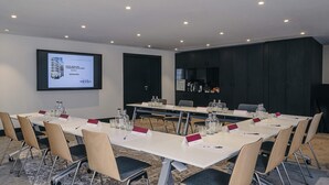 Un salón de conferencias con una mesa larga, sillas y una pantalla de proyector mostrando una presentación.
