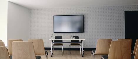 Un salón de conferencias con una gran pantalla plana montada en la pared, una mesa blanca con sillas y un papel tapiz decorado.