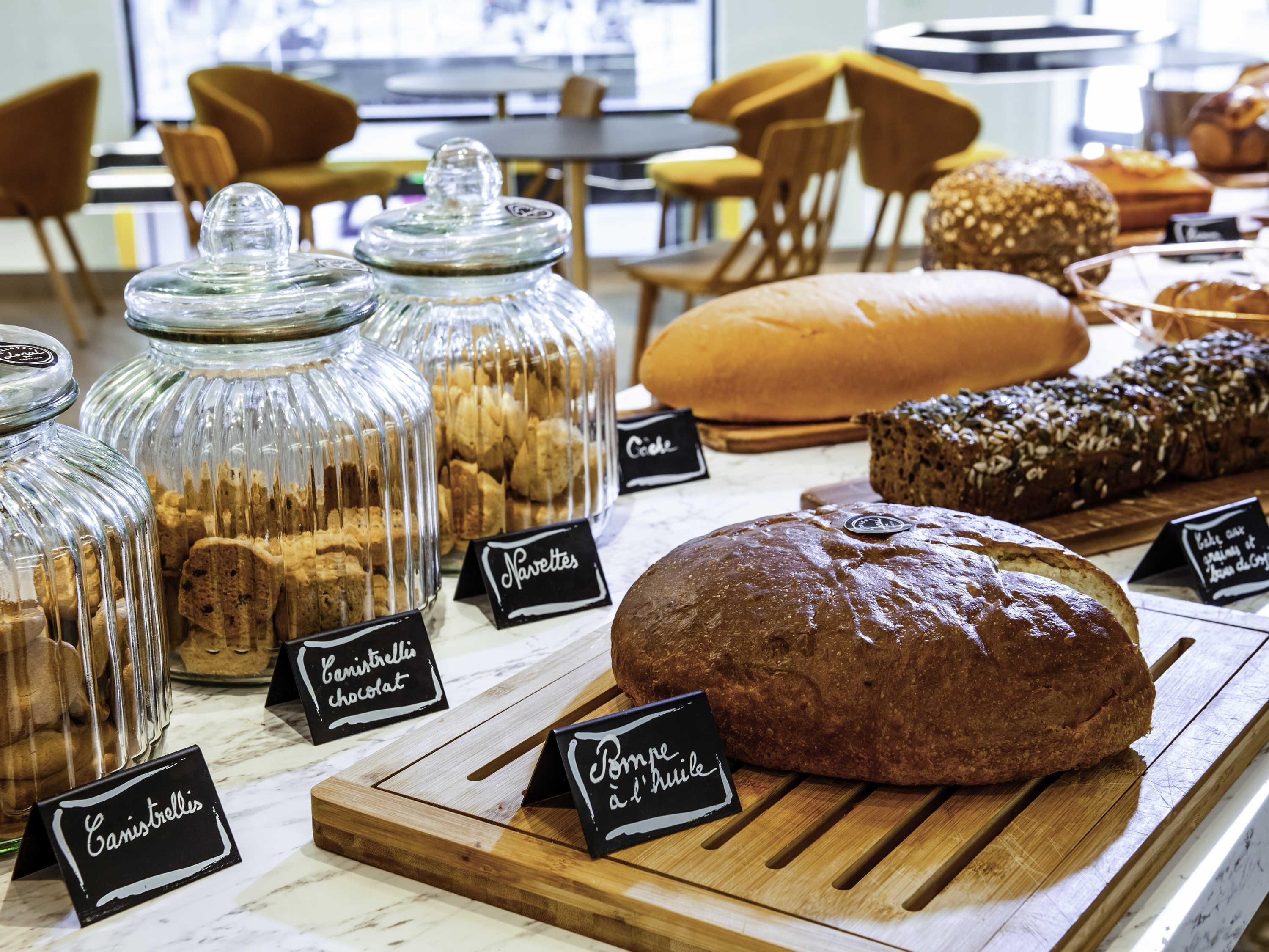 Une vitrine de boulangerie présentant diverses sortes de pains et de viennoiseries, dont une grande miche de pain étiquetée « Pain de mie ».