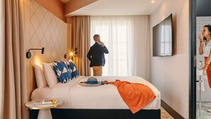 A hotel room with a bed, a small round table, a TV, and a bathroom with a mirror.