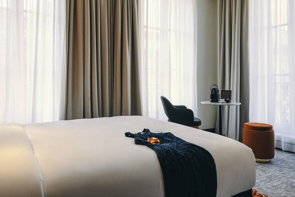 Ein Hotelzimmer mit einem großen Bett, einem Sessel, einem kleinen Tisch mit Kaffeemaschine und einem runden Hocker.