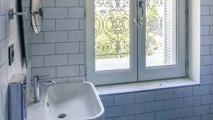 Un baño con lavamanos blanco, un espejo y una ventana con reja de metal.