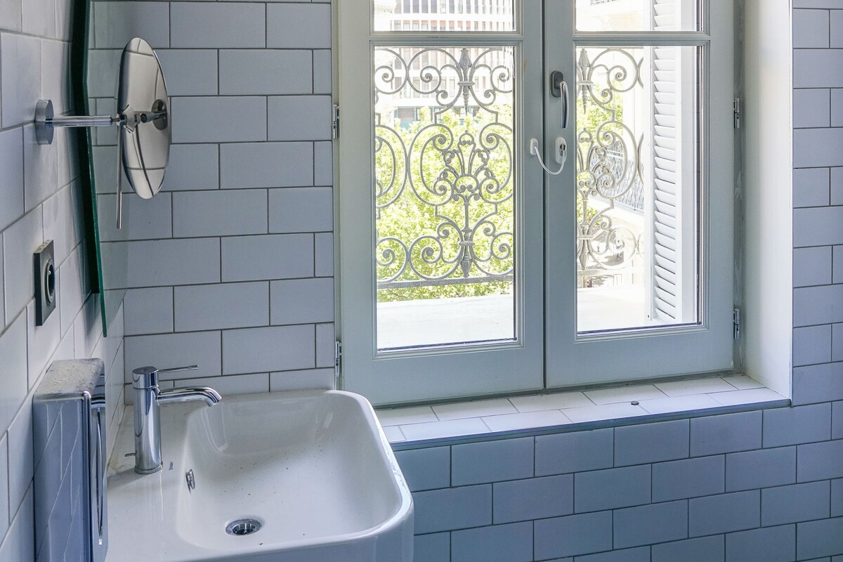 Un baño con lavamanos blanco, un espejo y una ventana con reja de metal.