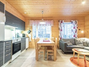 A modern kitchen with a dining area and a living room, featuring wooden walls and a large window.