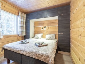 A bedroom with a bed, bedside tables, a window with curtains, and a wooden ceiling.