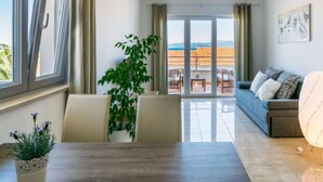Una sala de estar moderna con sofá, una mesa de comedor con sillas y un balcón con vista a la ciudad.