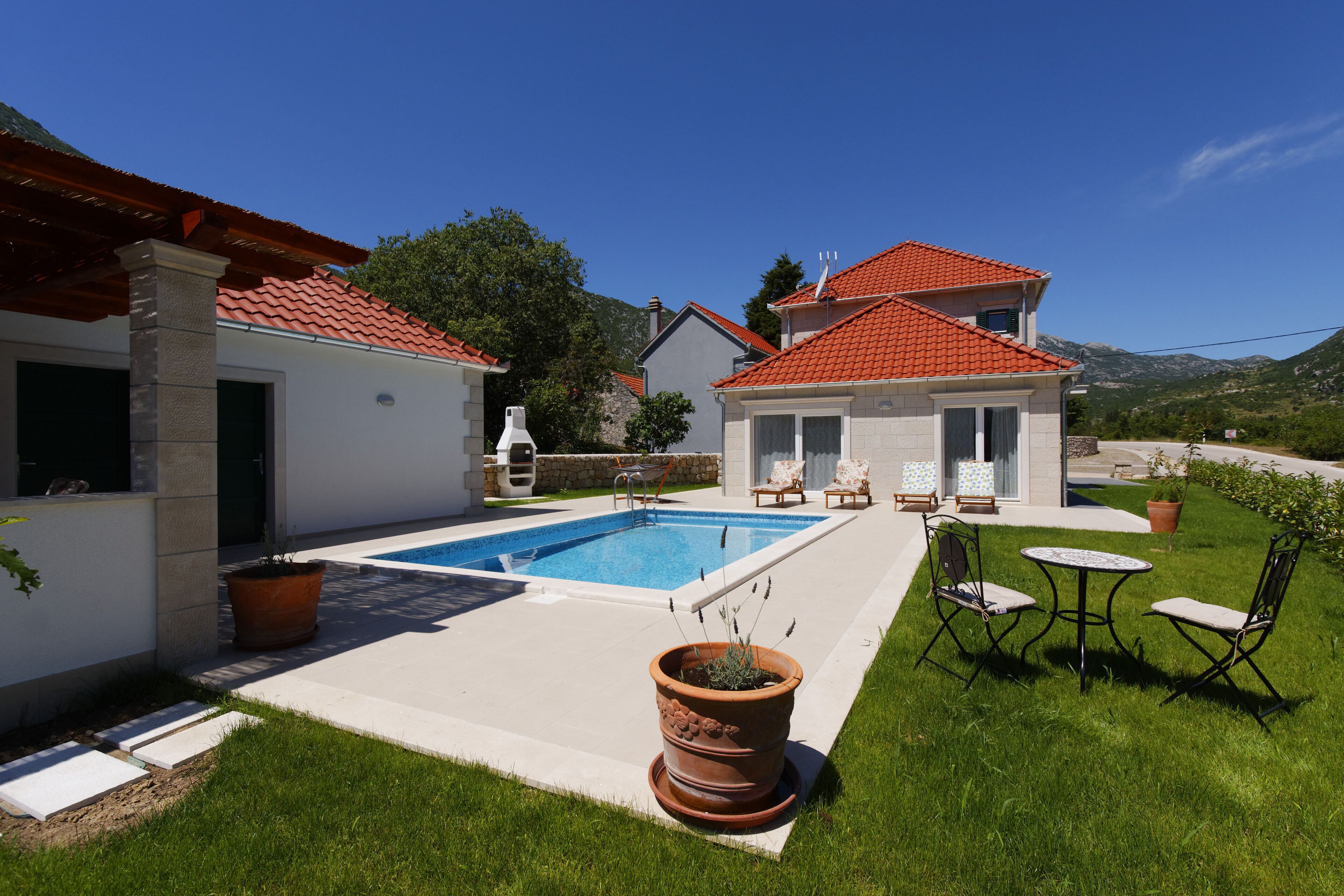 A residential property with a swimming pool, outdoor seating, and a well-maintained lawn.
