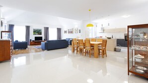A modern living room with a sofa, dining table, and chairs. There is a kitchen area with cabinets and a sink. - Villa Župa (Imotski)