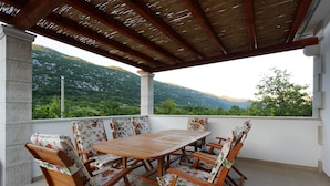 An outdoor patio with a wooden table and chairs, a pergola overhead, and a view of green hills and mountains. - Villa Župa (Imotski)