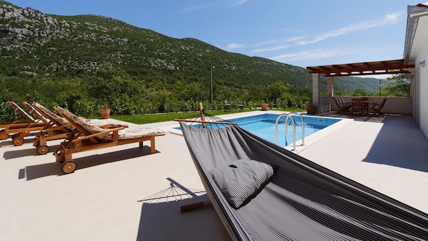 A pool area with lounge chairs and a hammock, overlooking a mountainous landscape. - Villa Župa (Imotski)