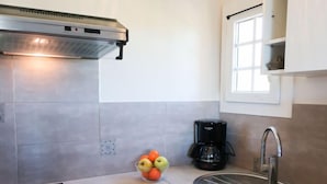 Una cocina moderna con baldosas grises, un lavamanos de acero inoxidable, una cafetera negra y un bol de fruta sobre la encimera.