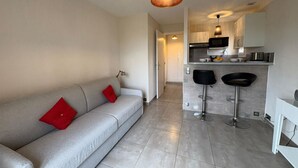 Una sala de estar moderna con un sofá gris, cojines rojos y una cocina con microondas, tostadora y dos taburetes negros.
