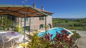 A villa with a stone exterior, a covered patio, a pool, and a table set for dining.