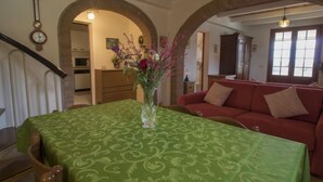 A dining area with a green table, a vase with flowers, a red sofa, and a staircase.