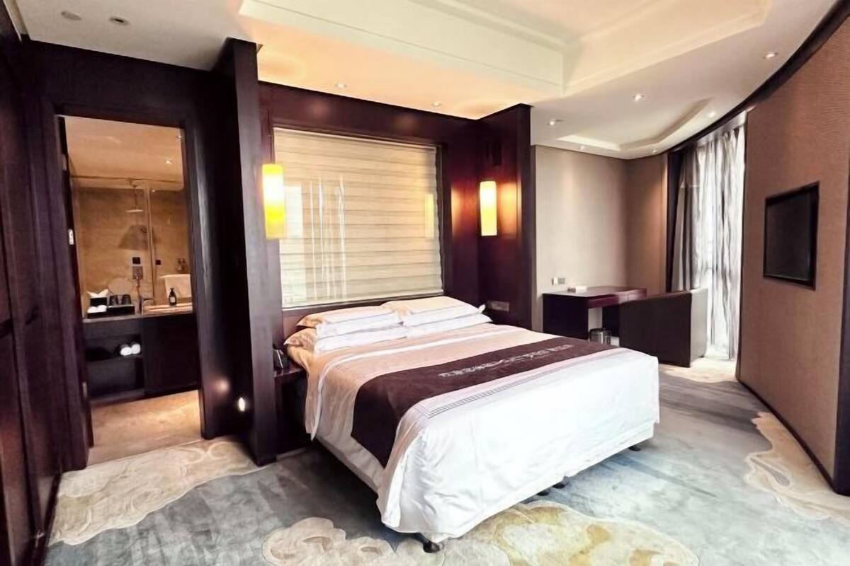 A hotel room with a large bed, a desk, a mirror, and a bathroom visible through an open door.