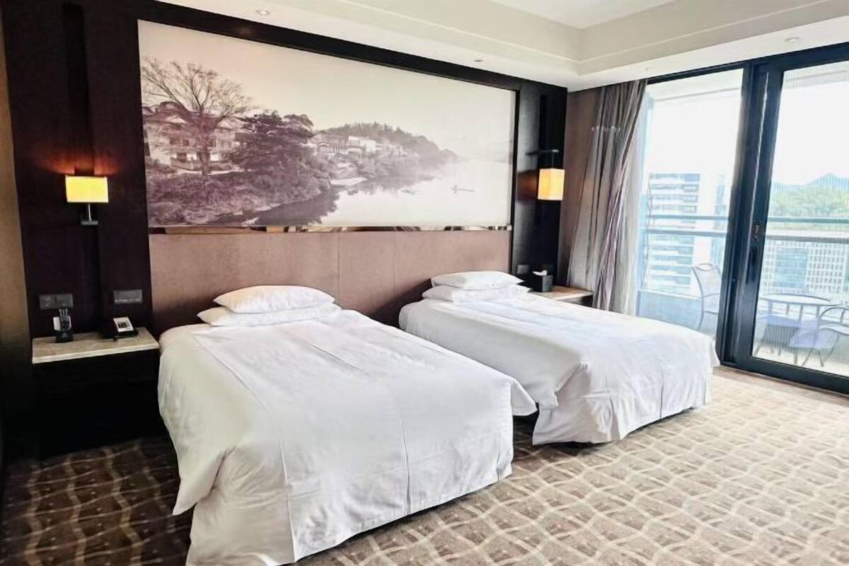 A hotel room with two beds, a large window, and a view of buildings.