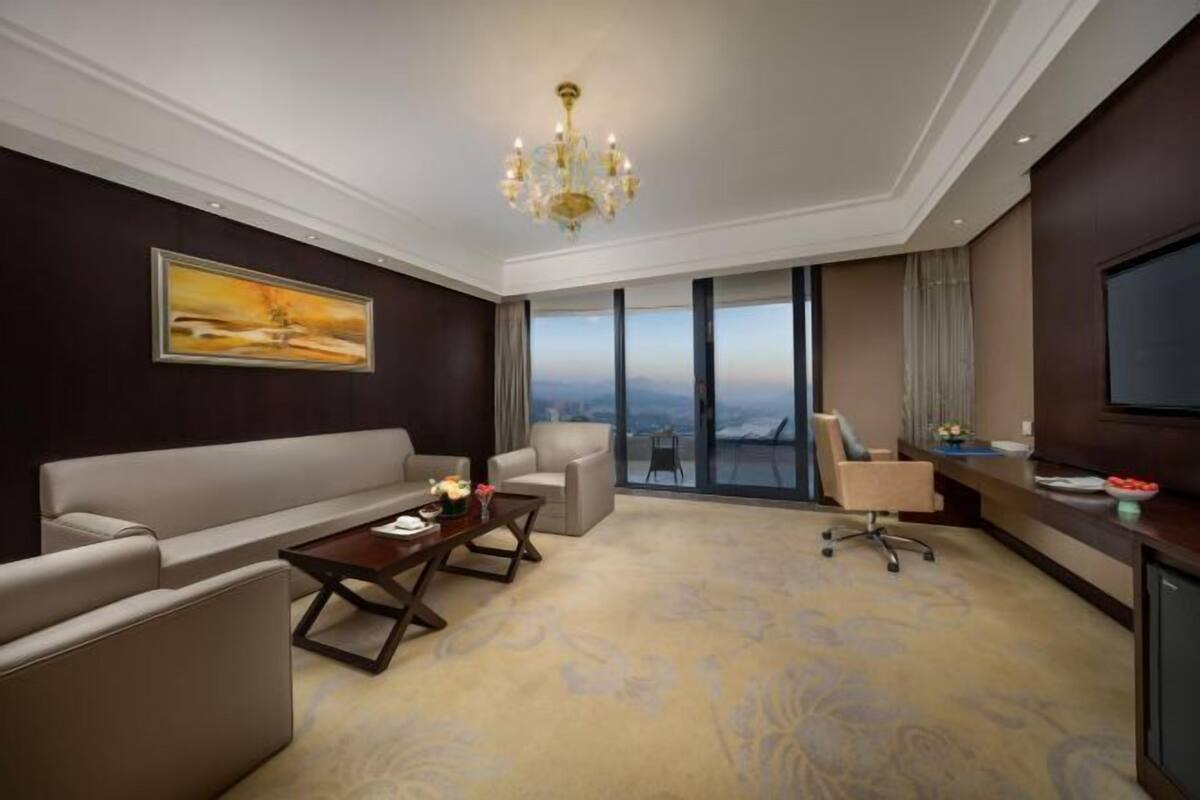 A modern hotel room with a large sofa, a coffee table, a desk, and a television.