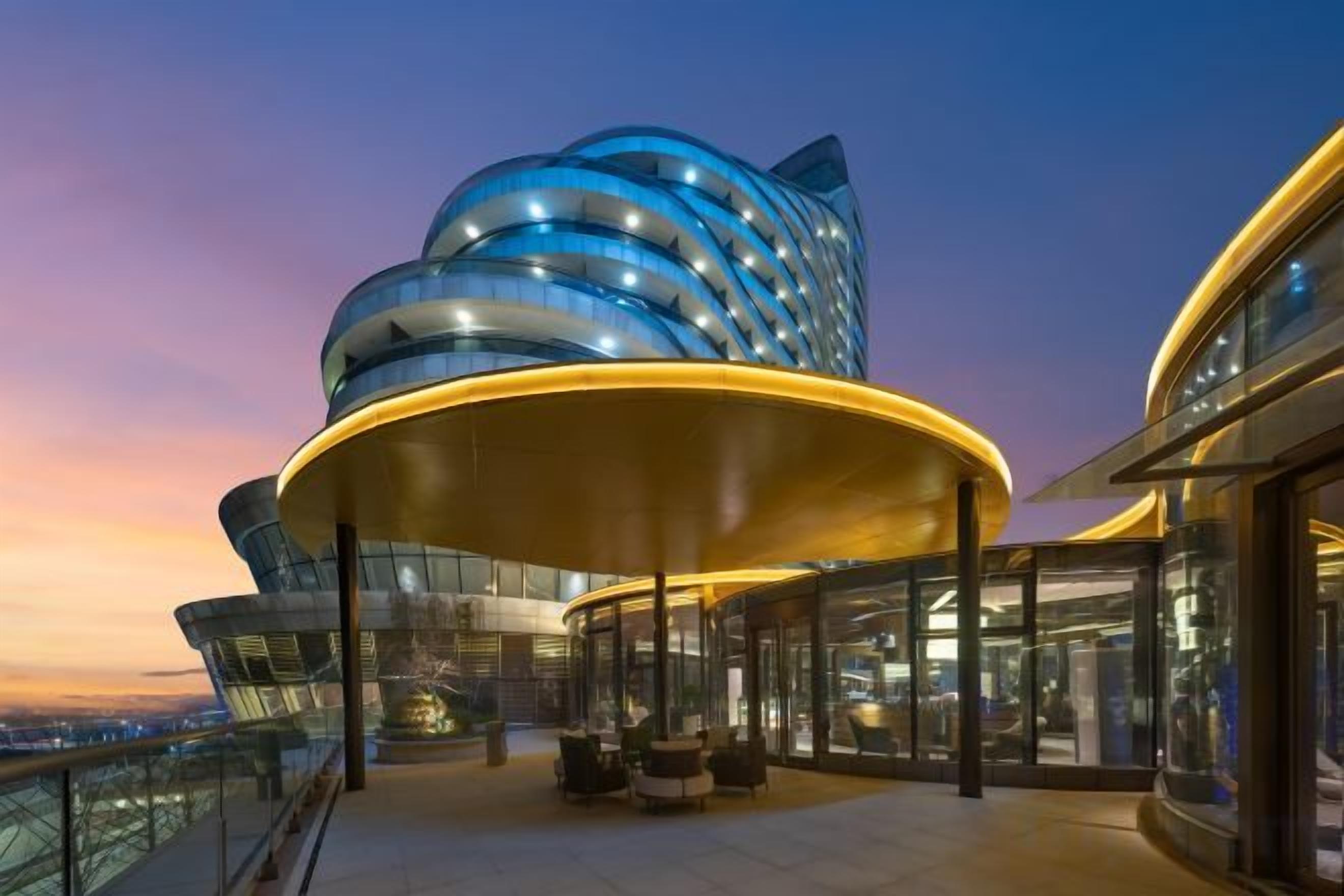 A modern building with a curved facade and a covered outdoor area with seating.